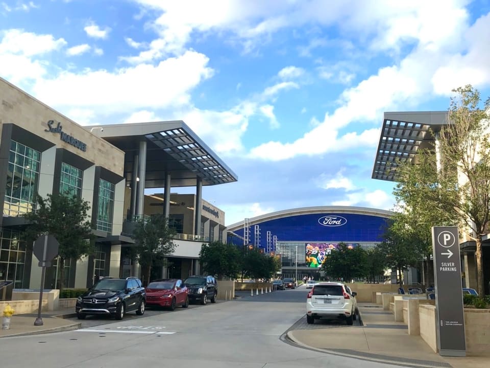 The Star in Frisco, Texas, with the domed Ford Center stadium and modern buildings of the Dallas Cowboys district under a blue sky.